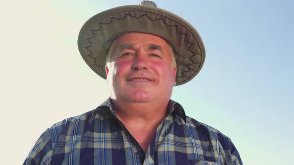 Content Mature Farmer in Countryside in Hat Looking at Camera