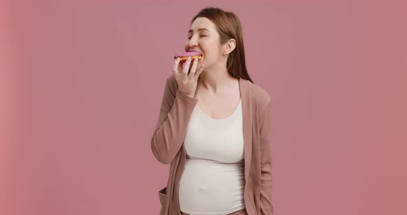 Young Happy Pregnant Woman Biting Sweet Donut Enjoying Junk Food Pink Studio Background