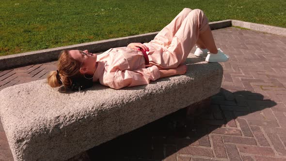 Tired, Caucasian Girl Lies- Resting on a Stone Bench on a Clear Sunny Day. The Concept of Fatigue