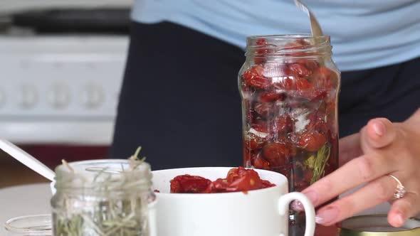 A Woman Lays Sun Dried Tomatoes In A Jar Of Olive Oil And Spices.