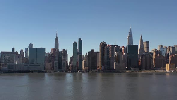 An aerial view over a calm East River on a sunny day with blue skies. The drone camera facing midtow