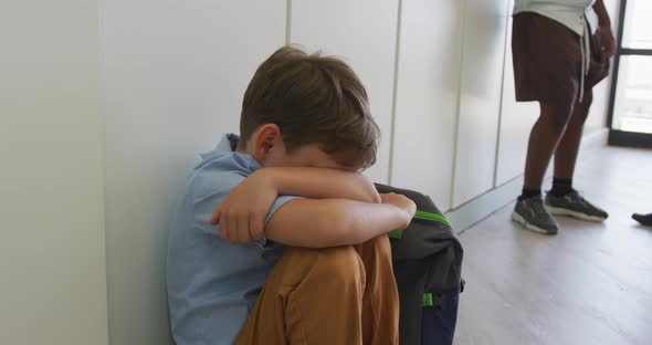 Video of sad caucasian boy sitting at school corridor, covering head with hands