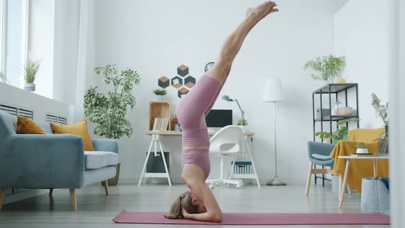 Side View of Attractive Girl Doing Headstand Concentrated on Yoga Activity in Apartment