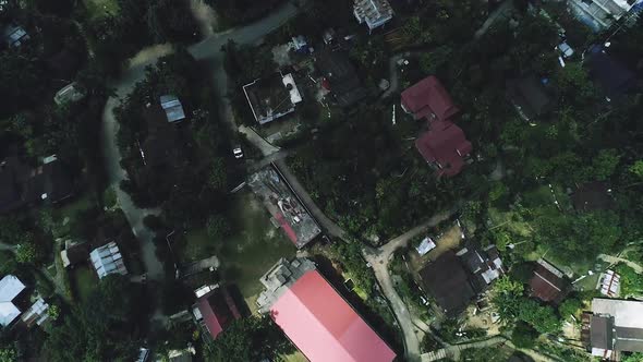 Top down view of village houses built on hill surrounded by lush vegetation and forest