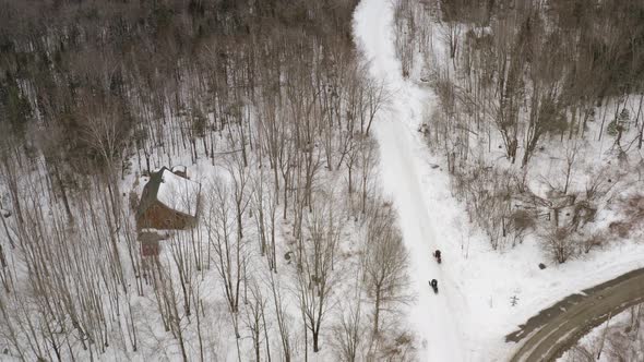 Snowmobiles stop along road outside house in wilderness Aerial view