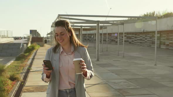 Portrait of smiling young woman with smartphone and coffee to go