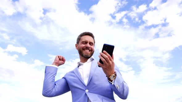 Excited Euphoric Broker Winner Looking at Smartphone Making Winning Gesture on Sky Mobile Bet