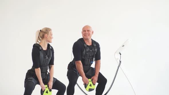 Fit Man and Woman in Electric Muscular Suit for Stimulation with Dumbbells