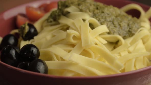 Serving of green pesto and tagliatelle pasta with black olives rotating medium shot