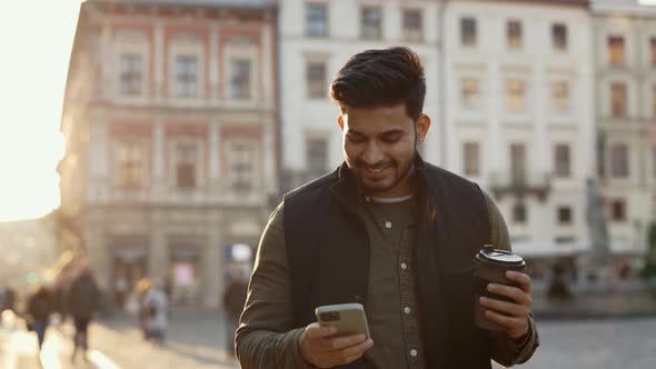 Indian Guy Walking on Street with Coffee and Mobile