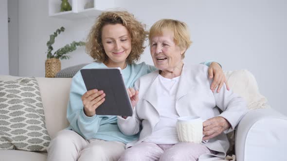 Granddaughter Teaching Grandmother How To Use A Tablet Computer