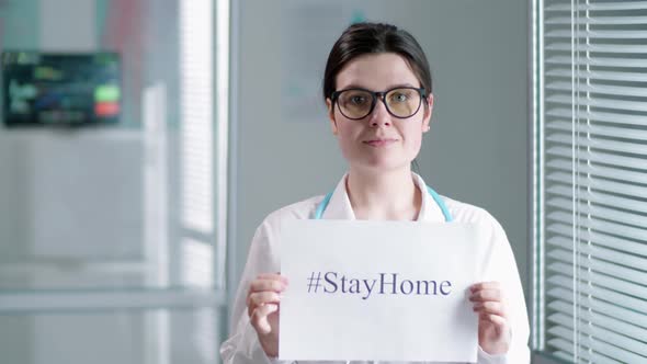 Young Female Doctor Holding Sheet of Paper with Stay Home Inscription