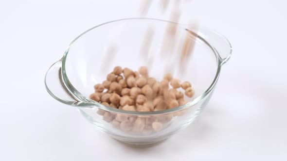 Dry raw chickpeas falling into a glass bowl on white background, slow motion