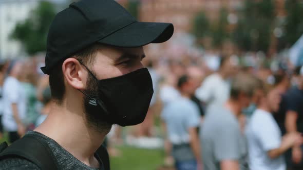 Portrait of male rebel activist in face mask marching in protesting riot crowd.