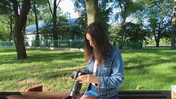 A Beautiful Young Girl is Sitting on a Bench in the Park Looking at Pictures