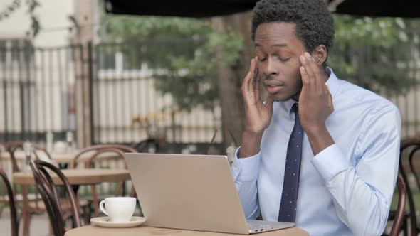 African Businessman with Headache Using Laptop in Outdoor Cafe