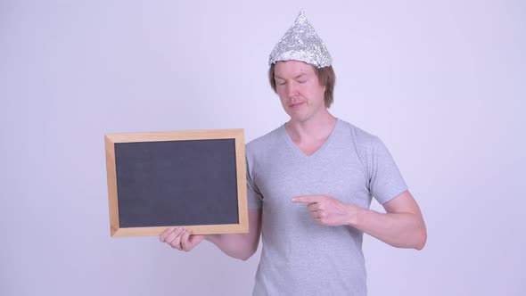 Young Man with Tinfoil Hat Holding and Pointing at Blackboard