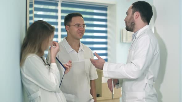 Male Doctor Holding Tablet Talking To Two Others Doctors in the Hospital Hall