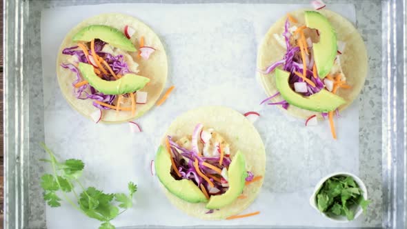 Preparing fresh fish tacos with cod and purple cabbage on a white corn tortillas.