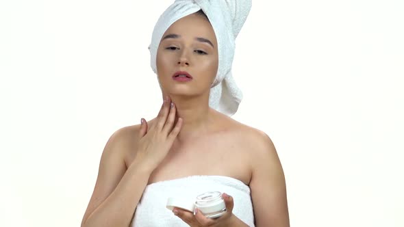 Portrait of Young Woman in White Towel on Her Head Applying a Cream on Her Previously Cleansed Face