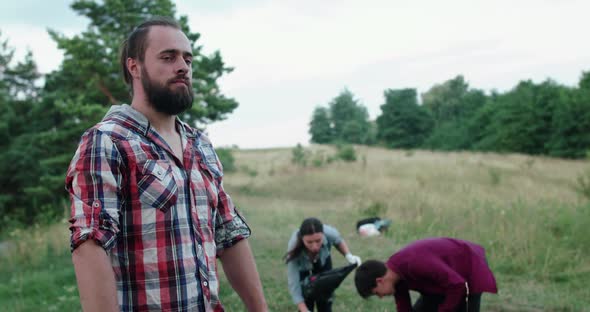 Portrait of Confident Man Looks and Crosses Hands at Camera at Workers on Nature