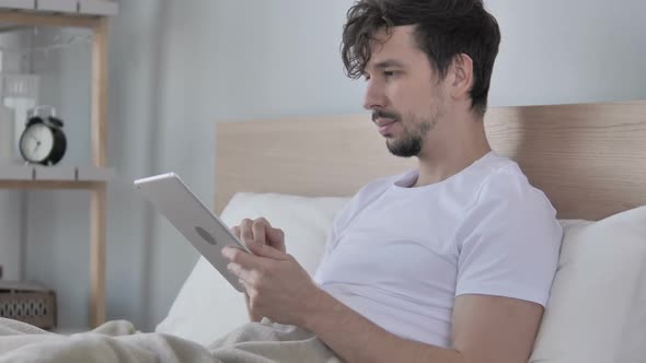 Online Video Chat on Tablet By Young Man in Bed