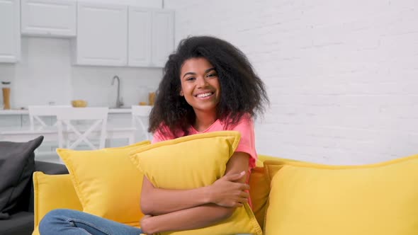 Smiling afro american woman sitting on the yellow sofa.