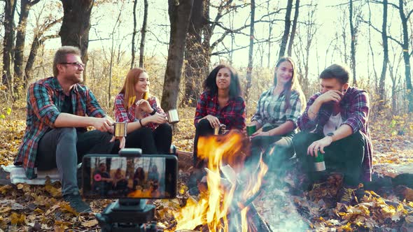 Travel bloggers sitting by campfire and streaming for social media