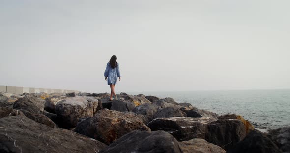 A Young Woman Walks Over Large Boulders Along the Coastline