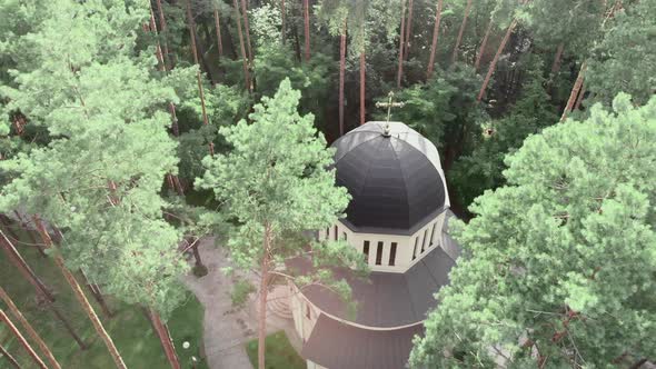 Aerial drone view of Christian church surrounded by green pine trees in forest at sunny day