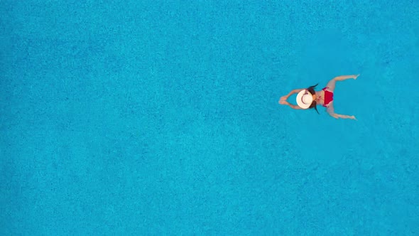 View From the Top As a Woman in Red Swimsuit and Hat Swims in the Pool