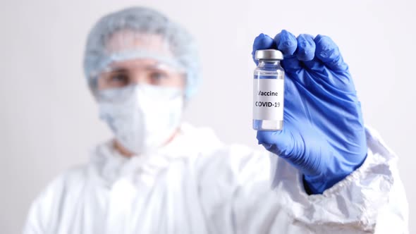 Medical Doctor in Protective Suit Holding Ampoule with Coronavirus Vaccine for COVID-19 Virus.
