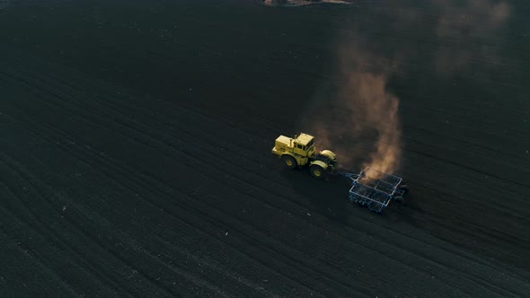 Tractor in the Large Brown Field Prepares the Soil for Sowing