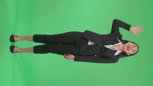 Full Body Of A Smiling Asian Business Woman Waving Hand And Say Hi While Standing On Green Screen