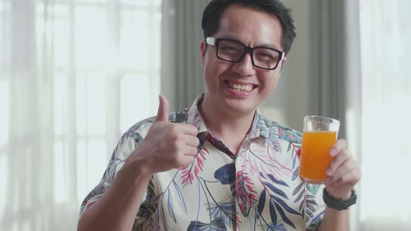 Close Up Of Smiling Asian Man Holding A Glass Of Orange Juice And Showing Thumbs Up