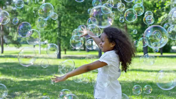 Little Girl and Boy Catching Soap Bubbles while Playing Outdoor