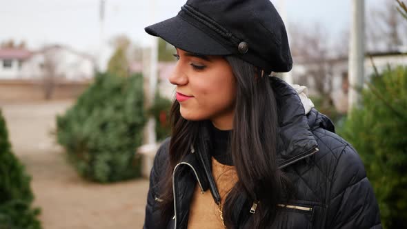 A beautiful hispanic woman shopping on a Christmas tree lot with green douglas fir conifers in a hol