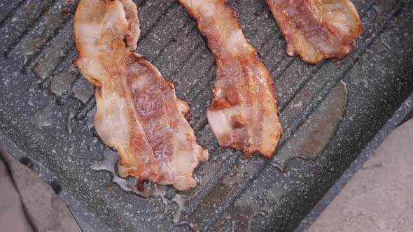 Cooking Pieces of Flavorful Sliced Organic Bacon Fried in Grill Pan