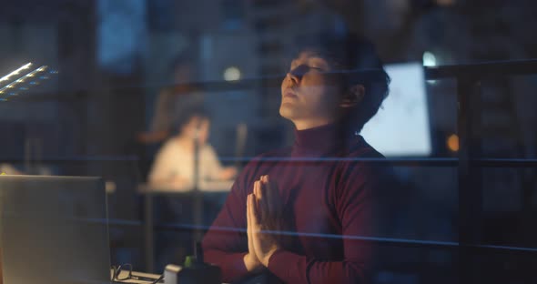 Stressed Asian Businessman Meditating in Yoga Pose in Night Office