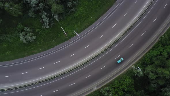 Cars and Trucks Move Along the Lanes of the Highway Among the Green Foliage  Rocket Drone Shot