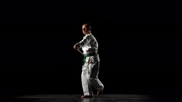 Kendo Fighter on White Kimono Practicing Martial Art with the Bamboo Bokken on Black Background.