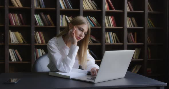 Business Woman in a White Shirt Works at a Laptop and Takes Notes