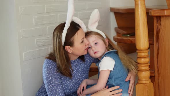 a Mother Soothes Her Crying Daughter on the Wooden Stairs of the House