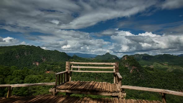 clouds moving over wooden bench in lush green mountainous scenery, time lapse