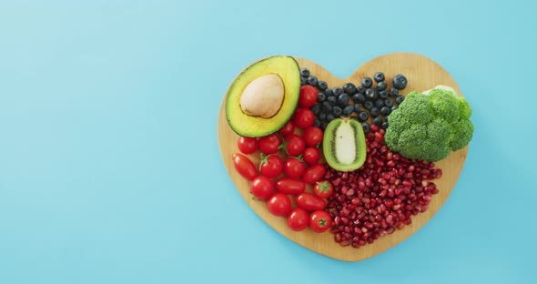 Video of fresh fruit and vegetables with copy space on heart shaped wooden board on blue background