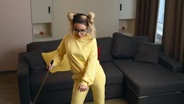 Happy Blonde Woman in a Yellow Hoodie with a Mop Cleaning the House and Dancing