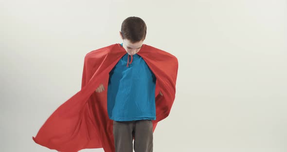 Boy with a superhero cape pretends to fly on a white studio background