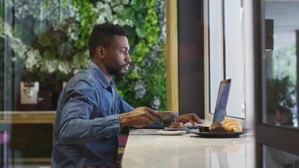 African american businessman using laptop drinking coffee in cafe