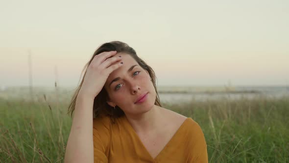 Portrait of young smiling woman sitting on a meadow in the evening