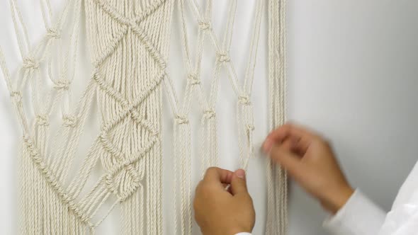 A woman weaves with her own hands a pattern of Macrame threads for decoration or home decor